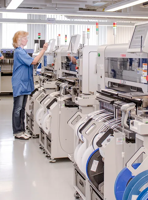 Female employee operates modern assembly machines in a bright electronics manufacturing facility.