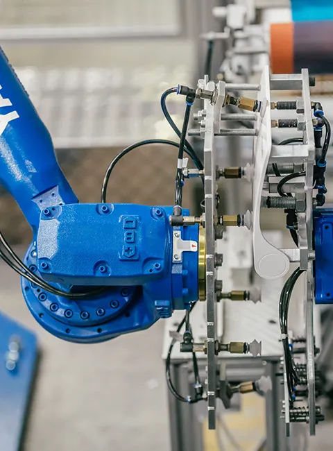 Blue industrial robot arm works on a rotating fixture in an automated manufacturing environment.