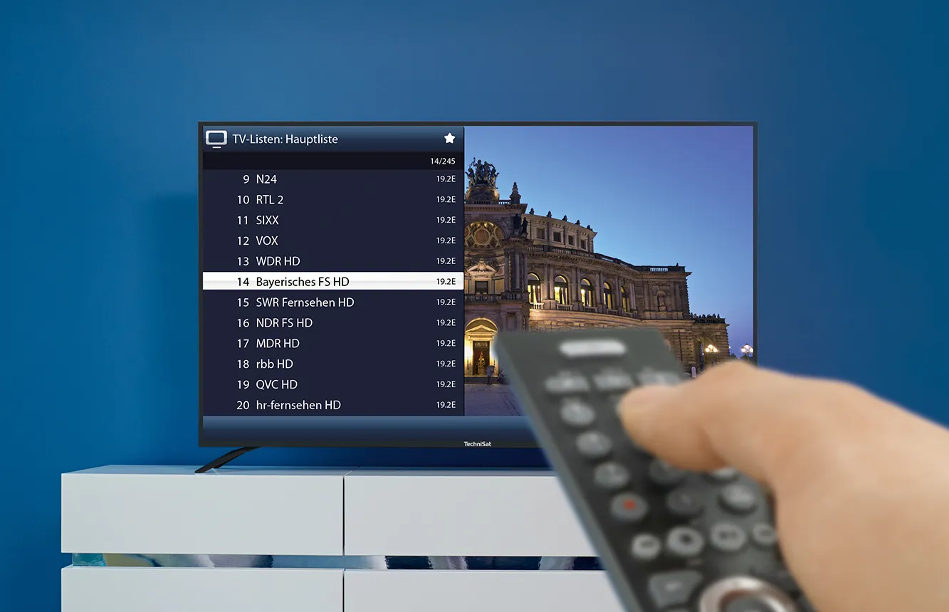 Eine Hand mit Fernbedienung vor einem Fernseher, auf dem eine TV-Senderliste angezeigt ist, ein HD-Sender ist ausgewählt.
