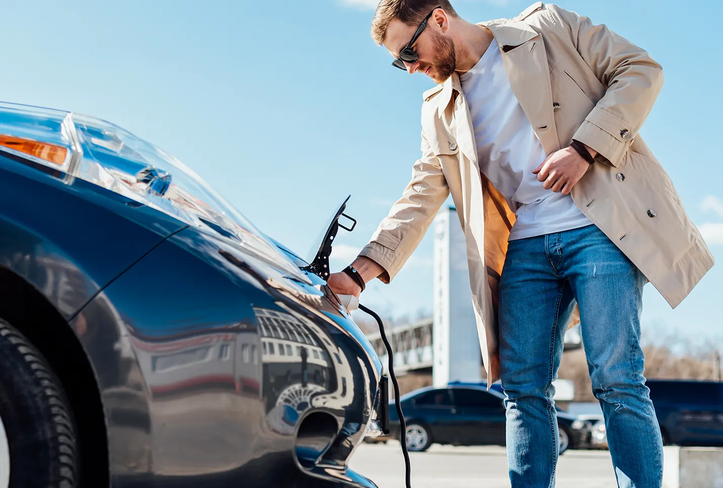 Ein Mann schließt sein Elektroauto mit einem Ladekabel an eine Wallbox an. Als Besucher nutzt er die Ladeoption.