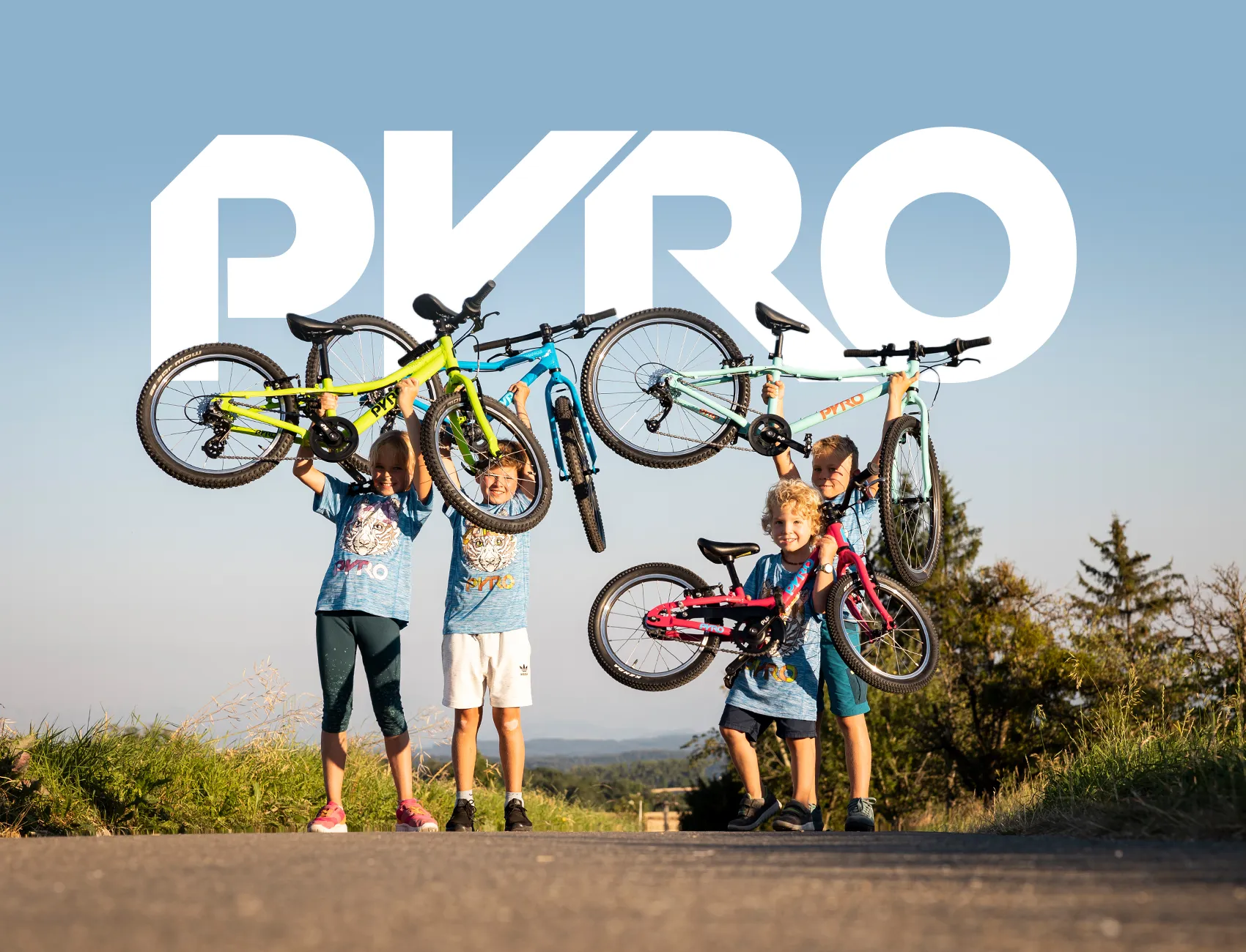 Abbildung von vier Kindern auf einem weiten Radweg. Jedes Kind präsentiert stolz ein zu seinem Alter passendes PYRO Kinderfahrrad in verschiedenen Farben.
